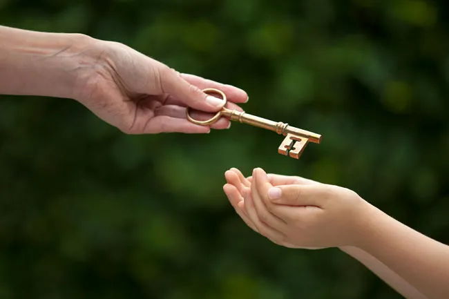 A key, representing the assets of a parent, being passed on to the beneficiary, which is what happens when a person has a sound estate plan, including a legally enforceable Will.