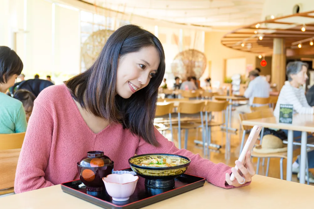 photo of a young Asian female in a coffee shop, on a video call with her spouse from Canada